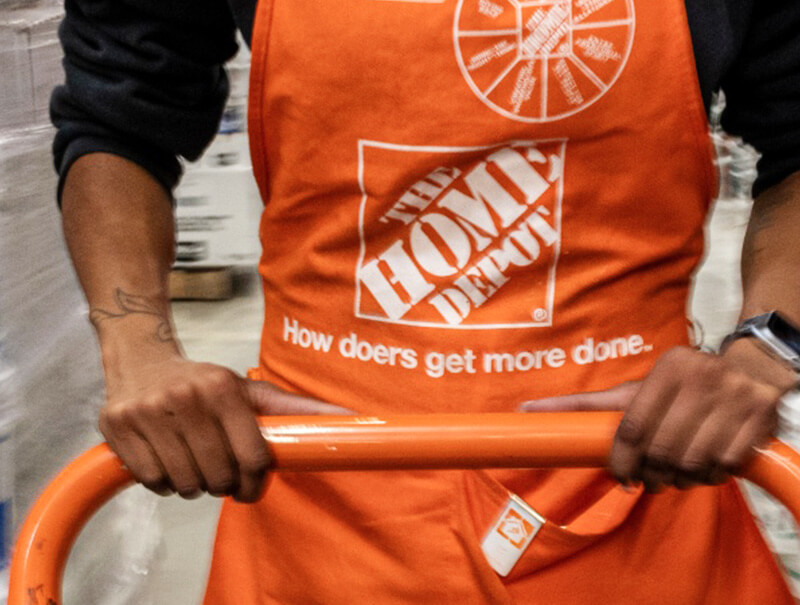 Zoomed in image of man with an orange "the home depot" apron on wheeling a cart